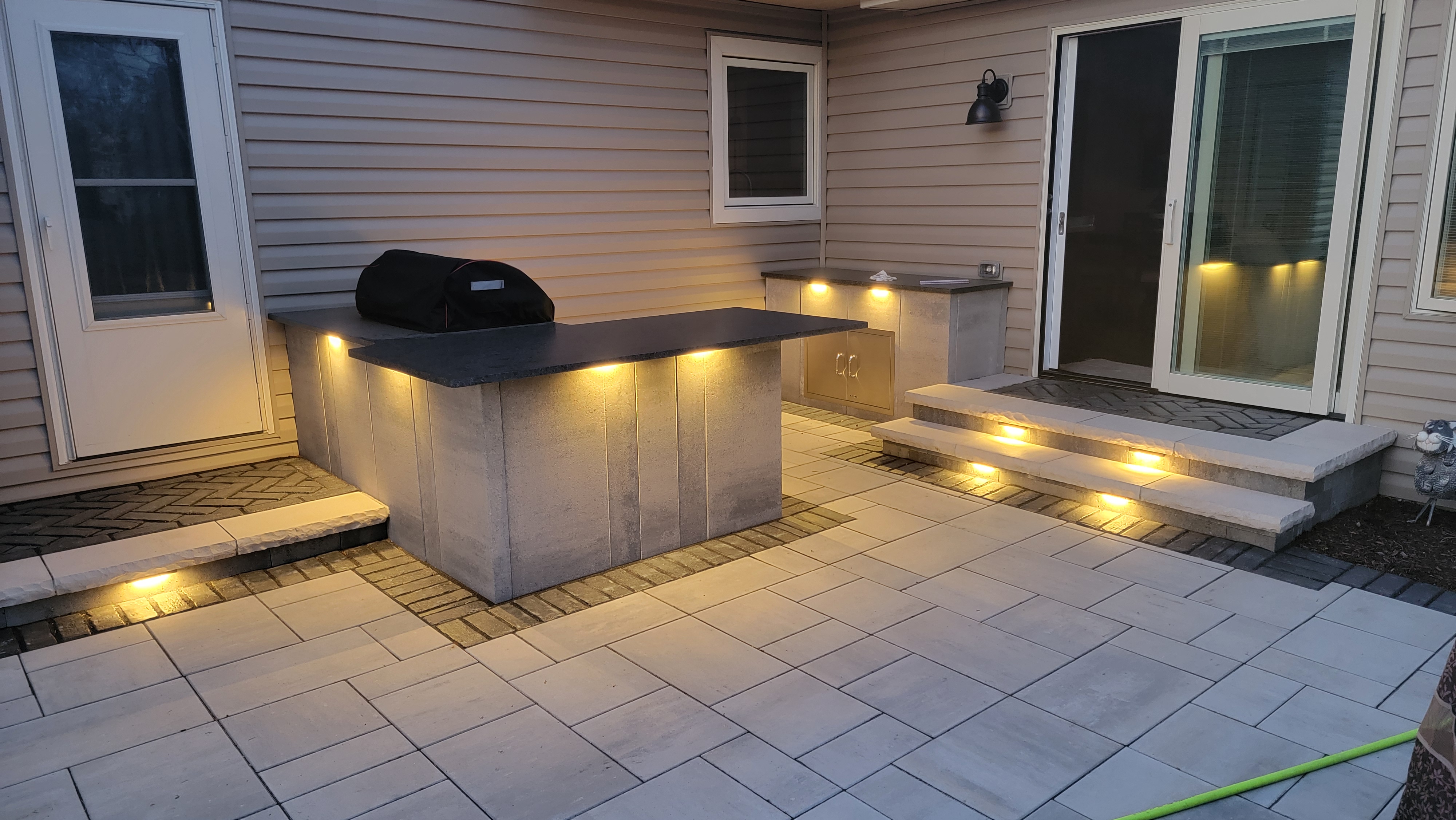 Paver patio with outdoor kitchen at night with landscape lights, Batavia, IL — B&L Landscape