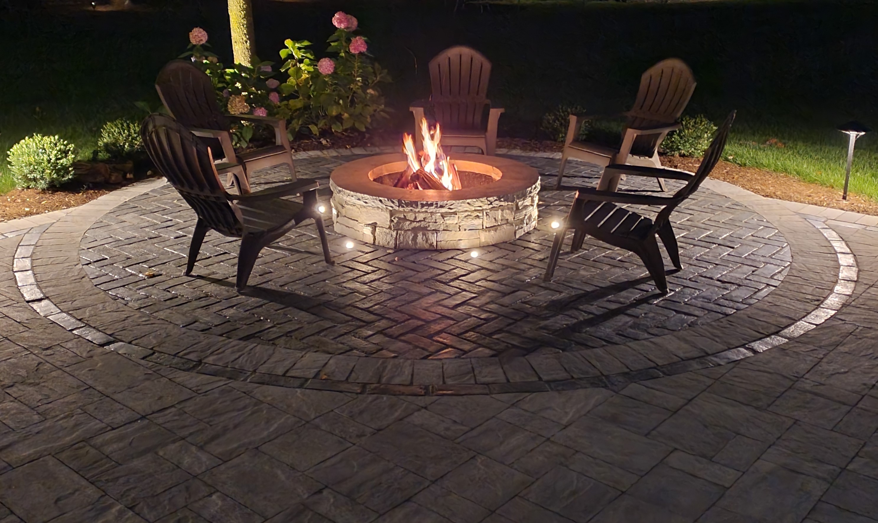 Rivercrest firepit with fire at night with up lights in bricks, Campton Hills, IL — B&L Landscape